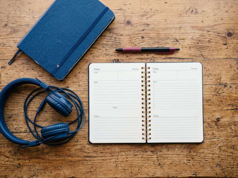 Mano escribiendo en una agenda junto a un cuaderno